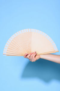 Close-up of woman holding hand fan against blue wall