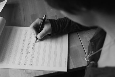 High angle view of woman writing in music sheet on table