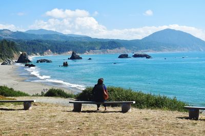 Rear view of man sitting on bench by sea against sky