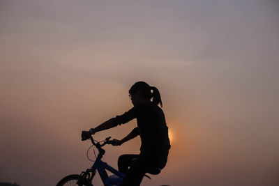 Silhouette man riding bicycle against sky during sunset