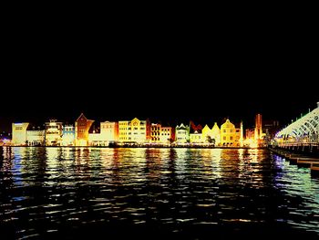 Illuminated city by water against clear sky at night