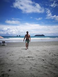 Full length of shirtless man walking at beach against sky