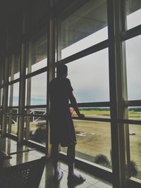 Rear view of man standing by window at airport