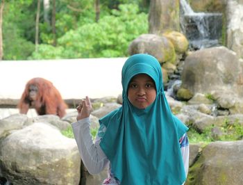 Portrait of girl wearing hijab pointing at orangutan at zoo