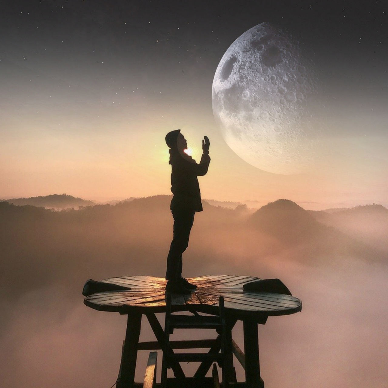 MAN STANDING ON MOUNTAIN AGAINST MOON AT SUNSET