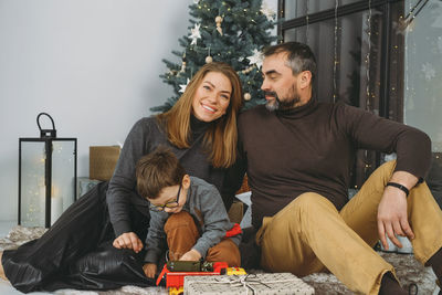 Family with child playing near christmas tree. child unpacking gifts, parents enjoy christmas tree