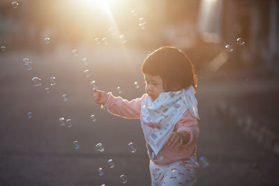 Cute girl looking at bubbles while standing on road