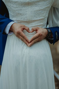 Midsection of groom making heart shape while embracing bride