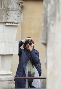 Woman photographing through camera while standing against wall
