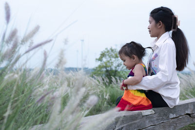 Side view of mother and daughter sitting on field