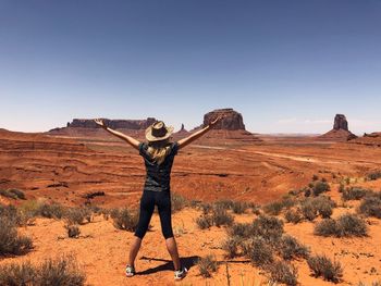 Woman with arms outstretched standing on dirt road against blue sky