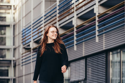 Portrait of young woman walking between modern buildings 