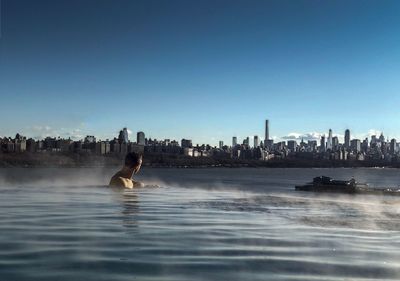 Man swimming in city against clear blue sky