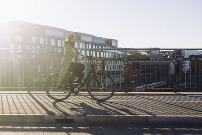 Full length side view of young businesswoman traveling through bicycle on road in city