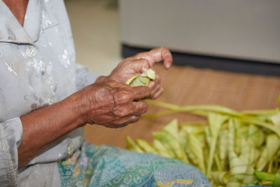 Hands of senior woman wrapping the sticky rice with palm leaf or ketupat palas