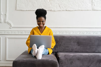 Close-up of smiling woman using laptop sitting on sofa at home