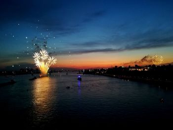 Firework display over river in city against sky