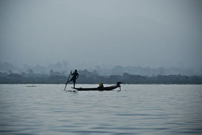 Boating in calm lake against clear sky