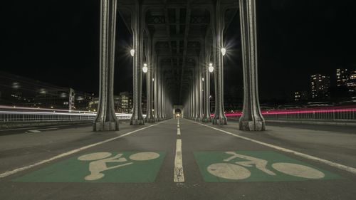 Diminishing perspective of illuminated bridge against sky in city at night