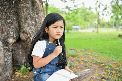 Thoughtful girl studying with sitting against tree at park