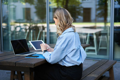 Rear view of woman using laptop while sitting on table