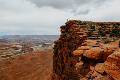 Man alone in far distance standing on large rock ledge over canyonland