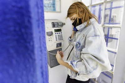 Side view of woman wearing mask talking on phone in booth