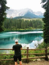 Rear view of man standing by lake against mountains