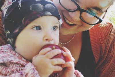 Close-up of happy mother looking at cute baby girl eating apple