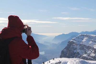 Man photographing on snowcapped mountains against sky