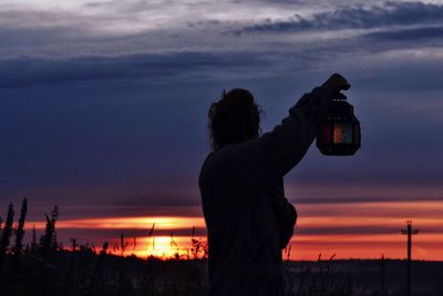Silhouette woman photographing sea against sky during sunset
