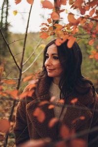 View of a brunette woman through branches and leaves in a forest in autumn.