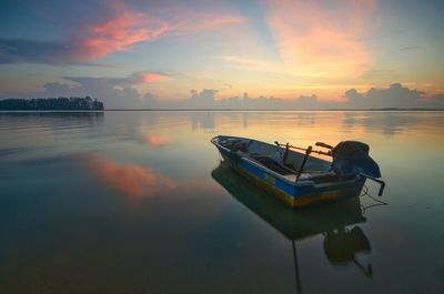 Boat moored in lake against sky during sunset