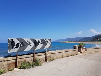 Scenic view of sign by sea against clear blue sky