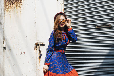 Young woman looking away while standing against shutter