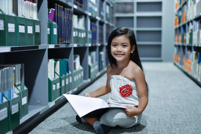 Portrait of smiling girl with book sitting in library
