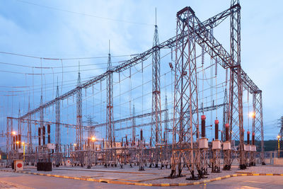 Illuminated electricity substation at dusk.