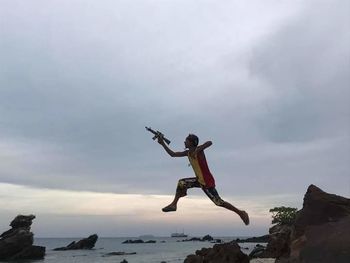 Man jumping on rock against sky