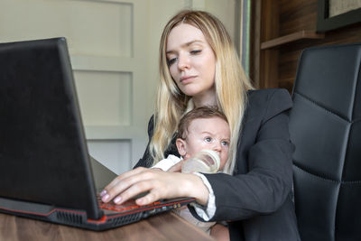 Young businesswoman holds baby in her arms, in office, combining this with working on laptop