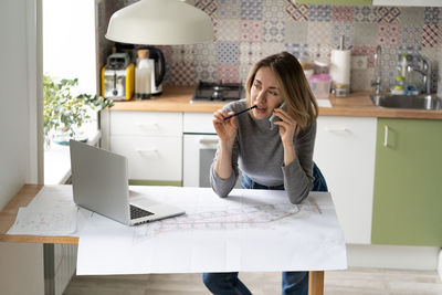 Female architect talking on phone while sitting at home