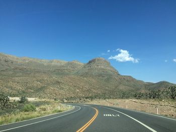 Road leading towards mountains against blue sky