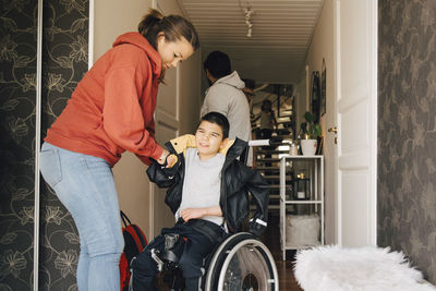 Mother assisting disabled son in wearing jacket at home