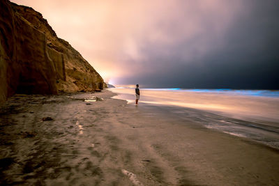 Man standing at beach against sky during sunset