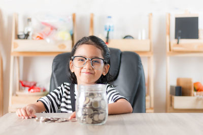 Portrait of girl sitting by coins at home