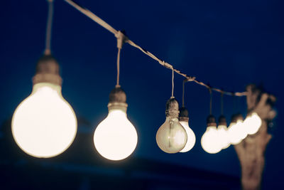 Low angle view of illuminated light bulbs hanging at night