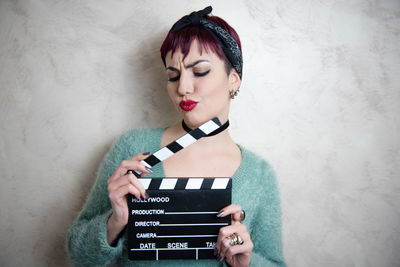 Young woman holding film slate against wall