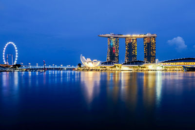 Marina bay sands by bay of water against sky in city at dusk
