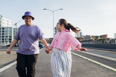 Brother and sister with down syndrome holding hands and walking on street