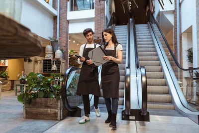 Male and female colleagues discussing while walking against escalator in boutique