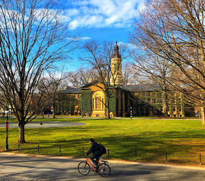 Man riding bicycle on street by building against sky